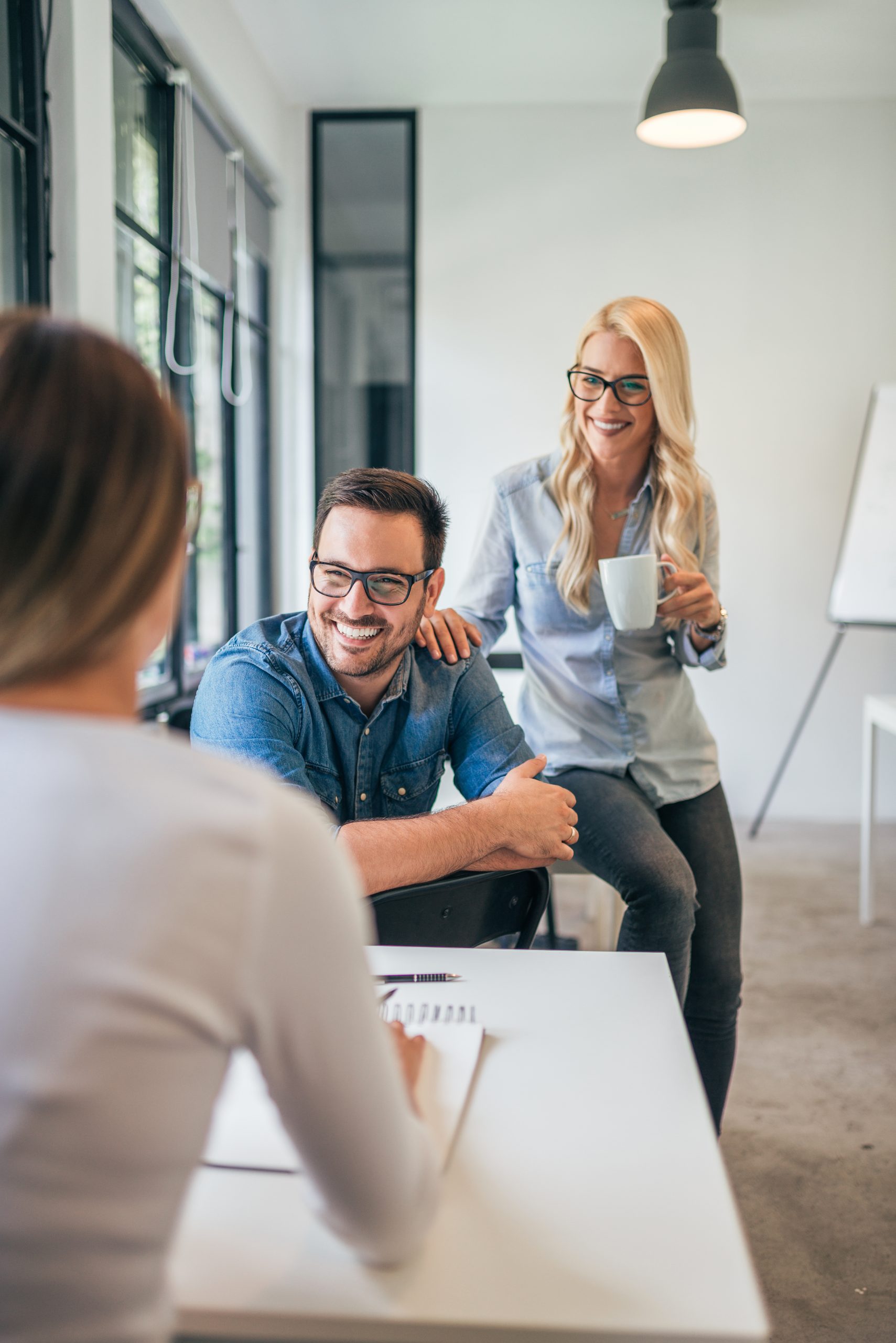 Three colleagues in modern co-working space or classroom talking and smiling.